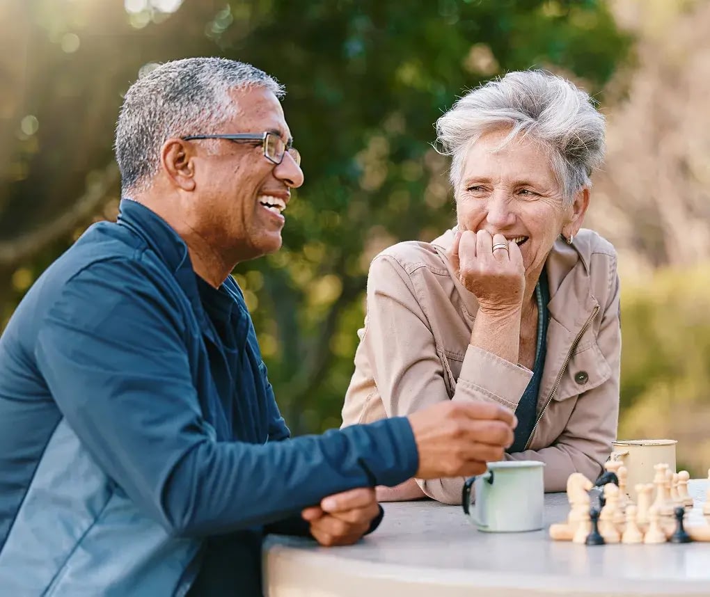 Two seniors laughing while playing chess outdoors