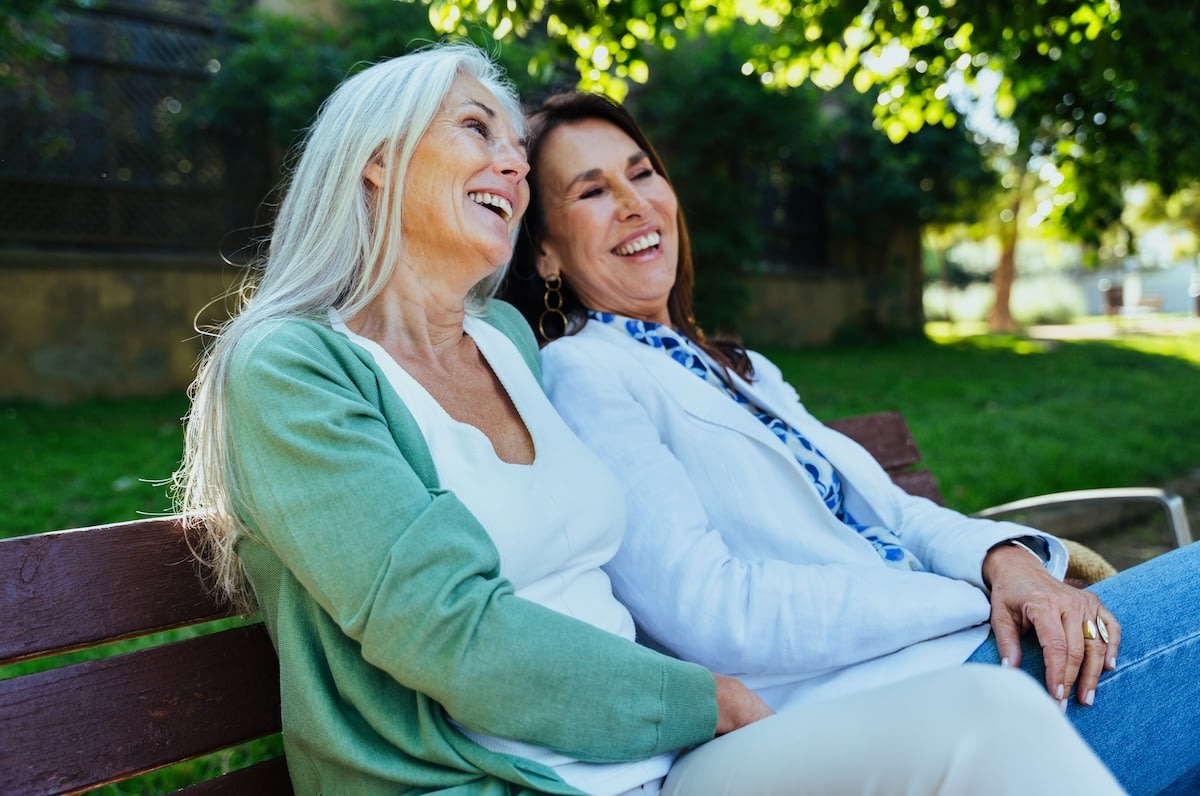 Two women laughing together on a park bench