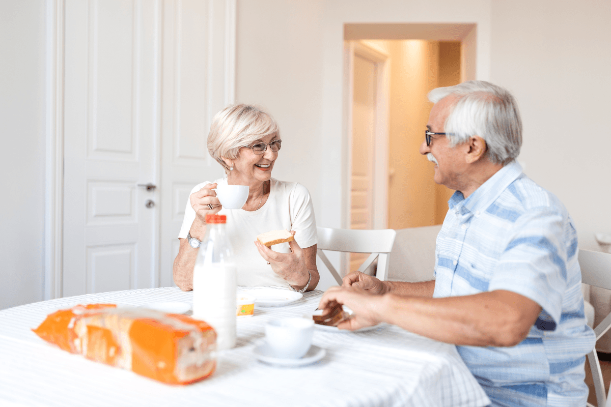 Happy senior couple talking and laughing during breakfast with coffee and milk.