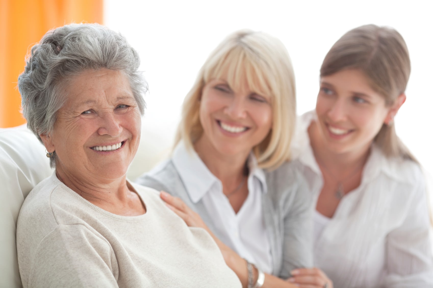 A senior woman and her two adult daughters smile warmly.