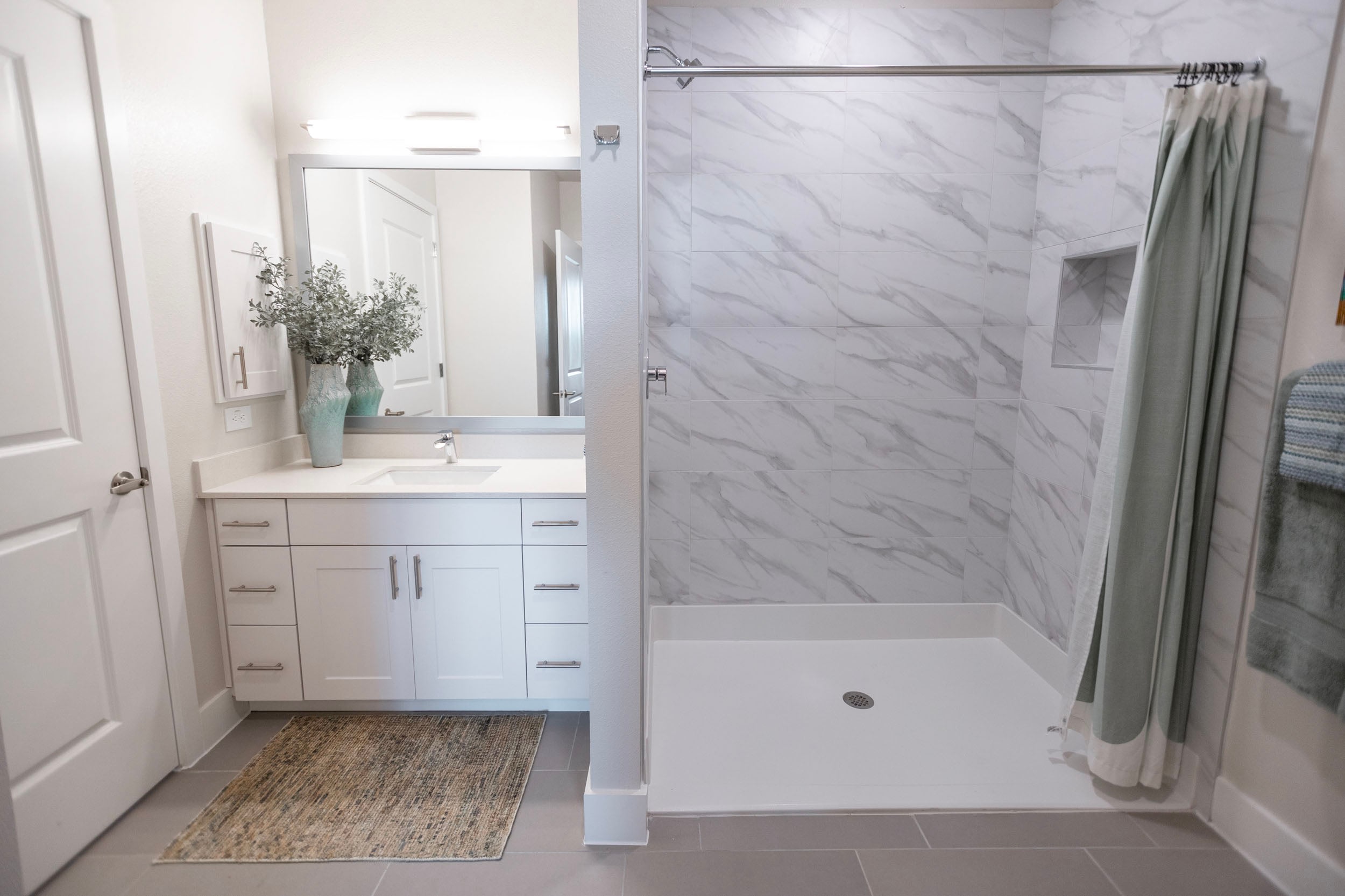 Modern bathroom interior featuring a spacious shower with marble tile, a sleek vanity with a sink, decorative plants, and neutral color tones. The design emphasizes functionality and contemporary aesthetics.