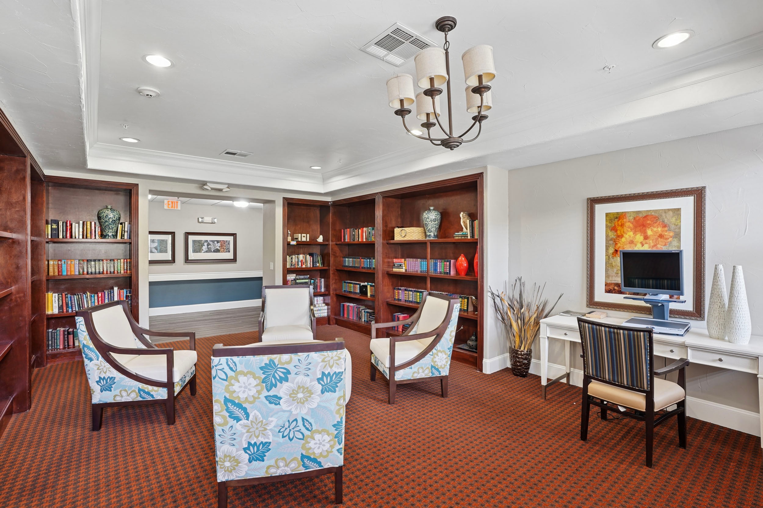 Cozy reading room featuring comfortable chairs, bookshelves filled with books, a desk with a computer, and decorative accents, ideal for relaxation and study.