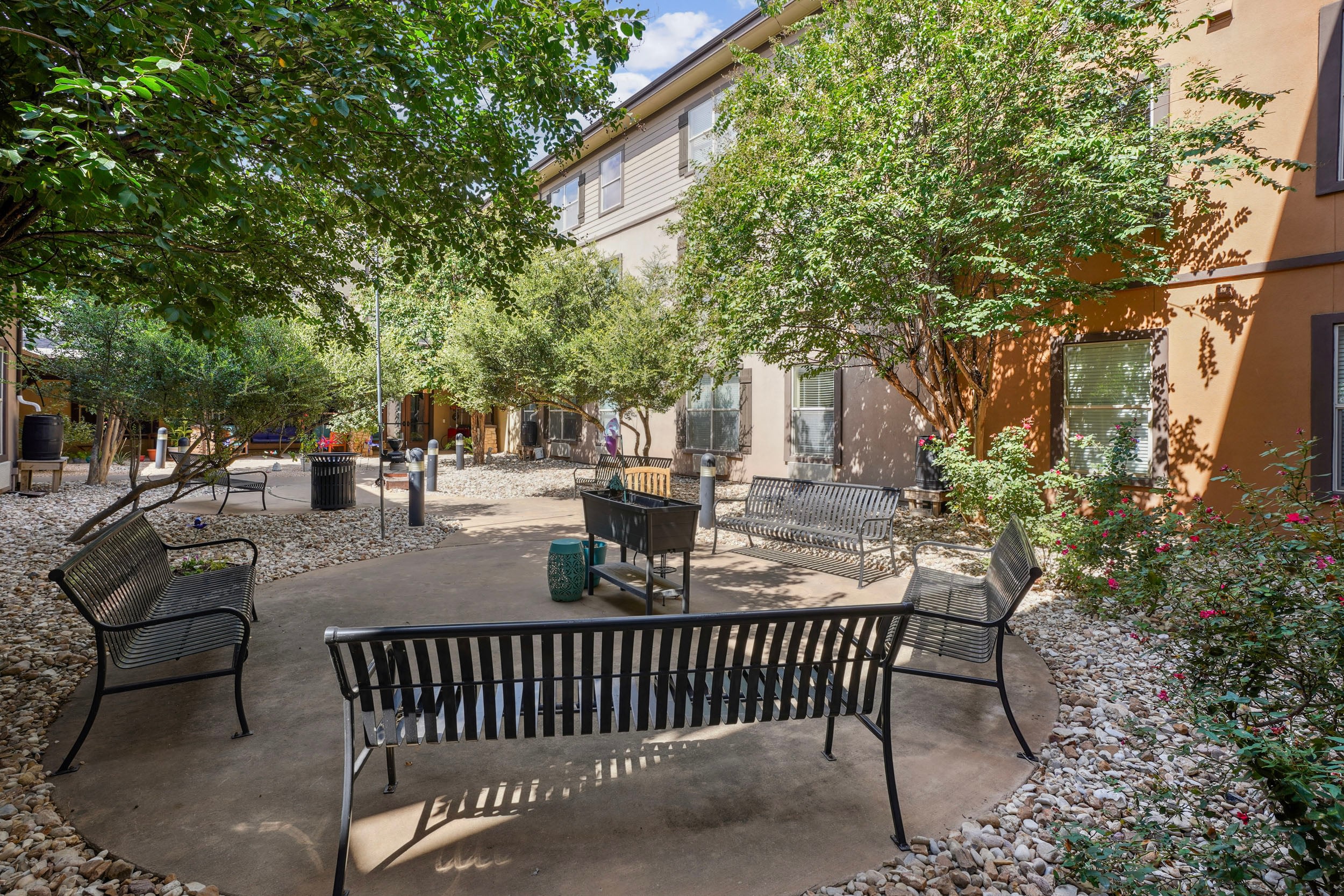 Lush outdoor courtyard featuring several black benches, surrounded by greenery and decorative rocks, ideal for relaxation and social gatherings in a residential setting.