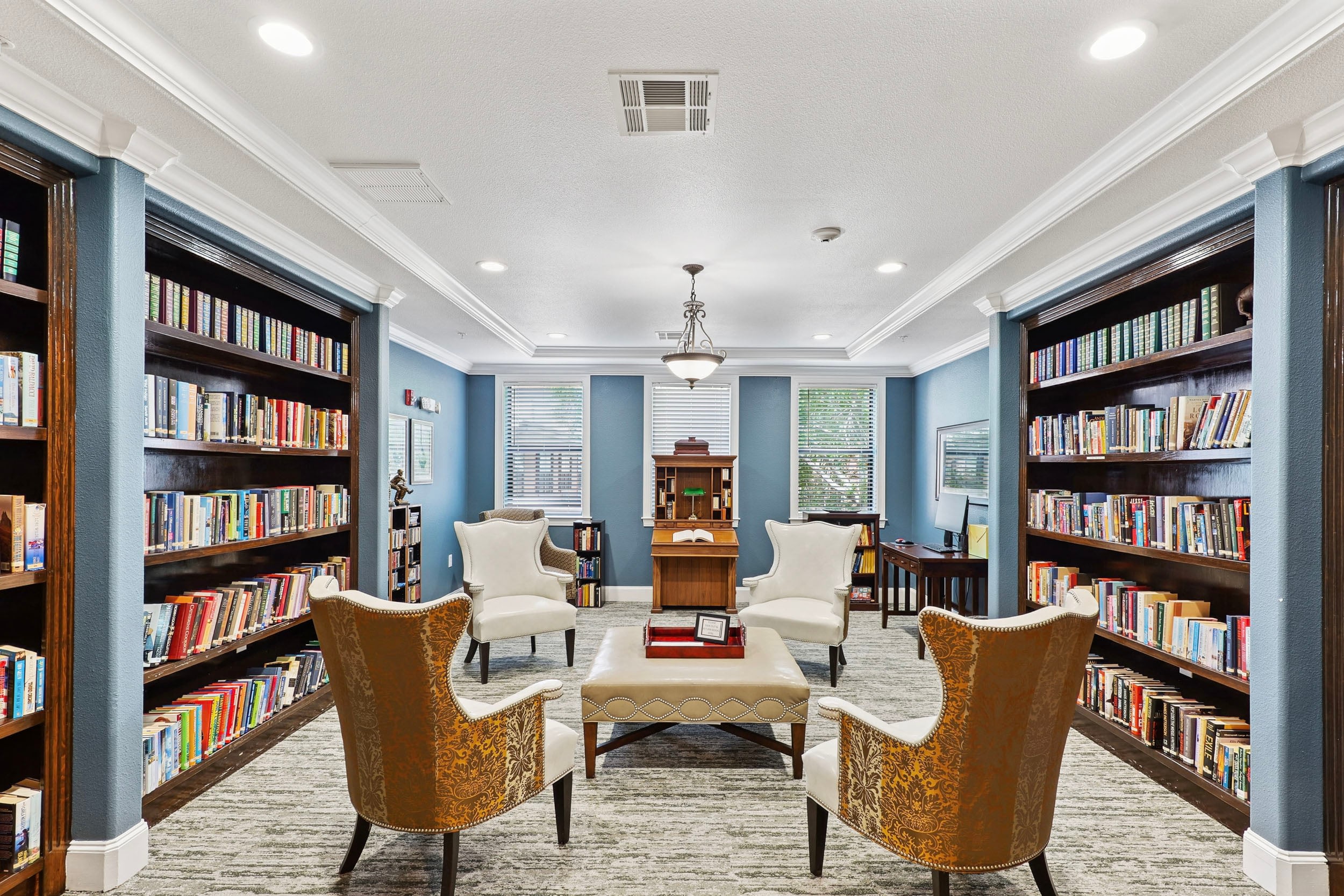 Cozy library interior featuring two elegant armchairs, a central coffee table, and bookshelves filled with a variety of books. Natural light streams through windows, enhancing the inviting atmosphere.