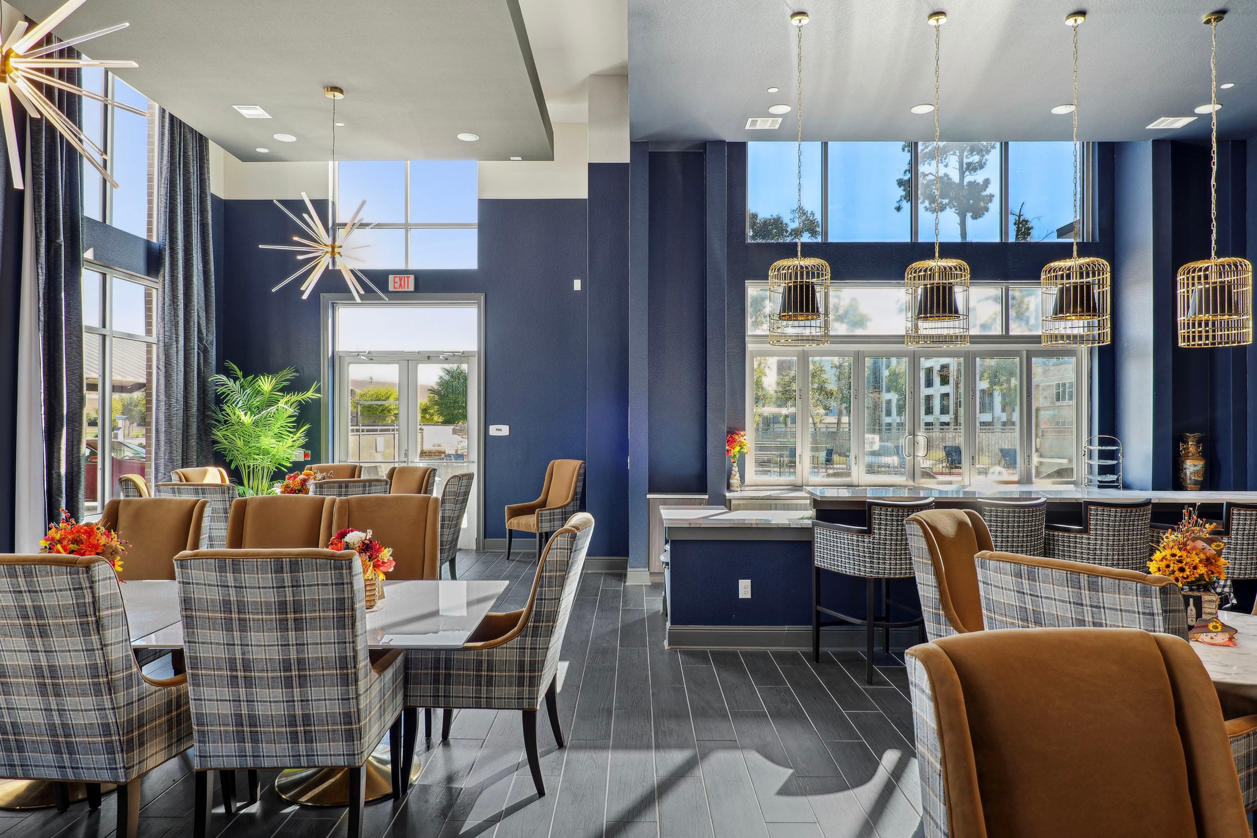 Modern dining area featuring stylish furniture, large windows, and elegant lighting fixtures. The space is decorated with plants and floral centerpieces, creating a welcoming atmosphere perfect for gatherings or meals.