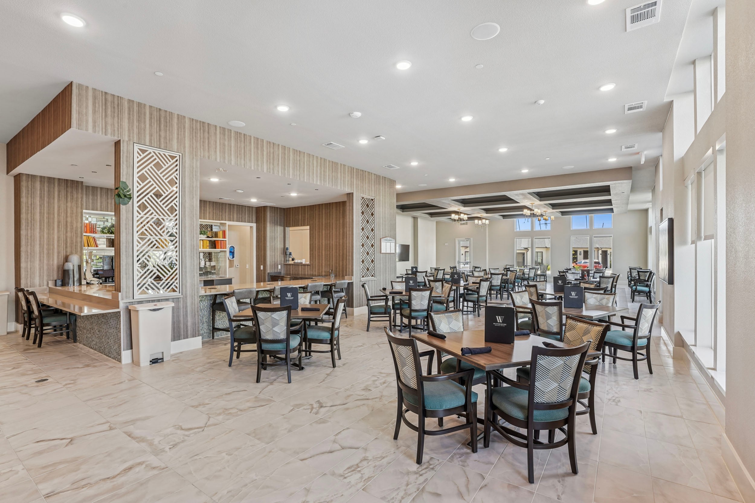 Modern dining area with elegant decor, featuring tables and chairs arranged for guests, large windows allowing natural light, and a stylish bar counter in the background.
