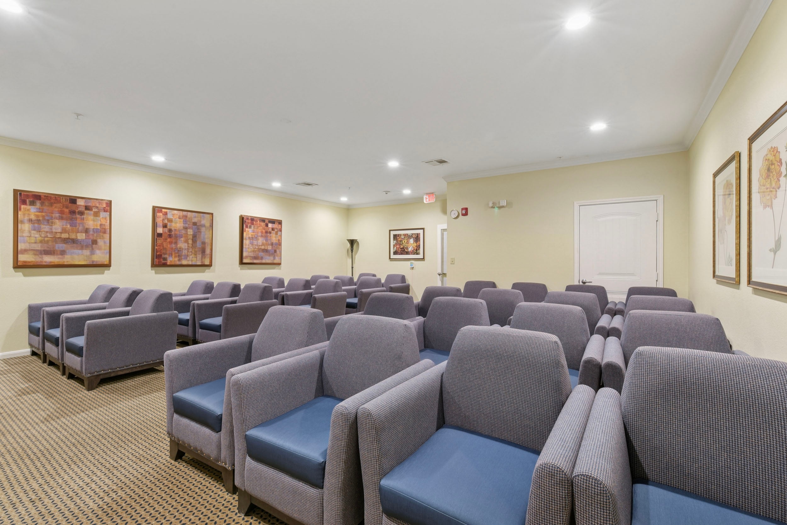 Waiting room with gray upholstered chairs arranged in rows, featuring modern artwork on the walls and neutral-colored decor, designed for comfort and relaxation.