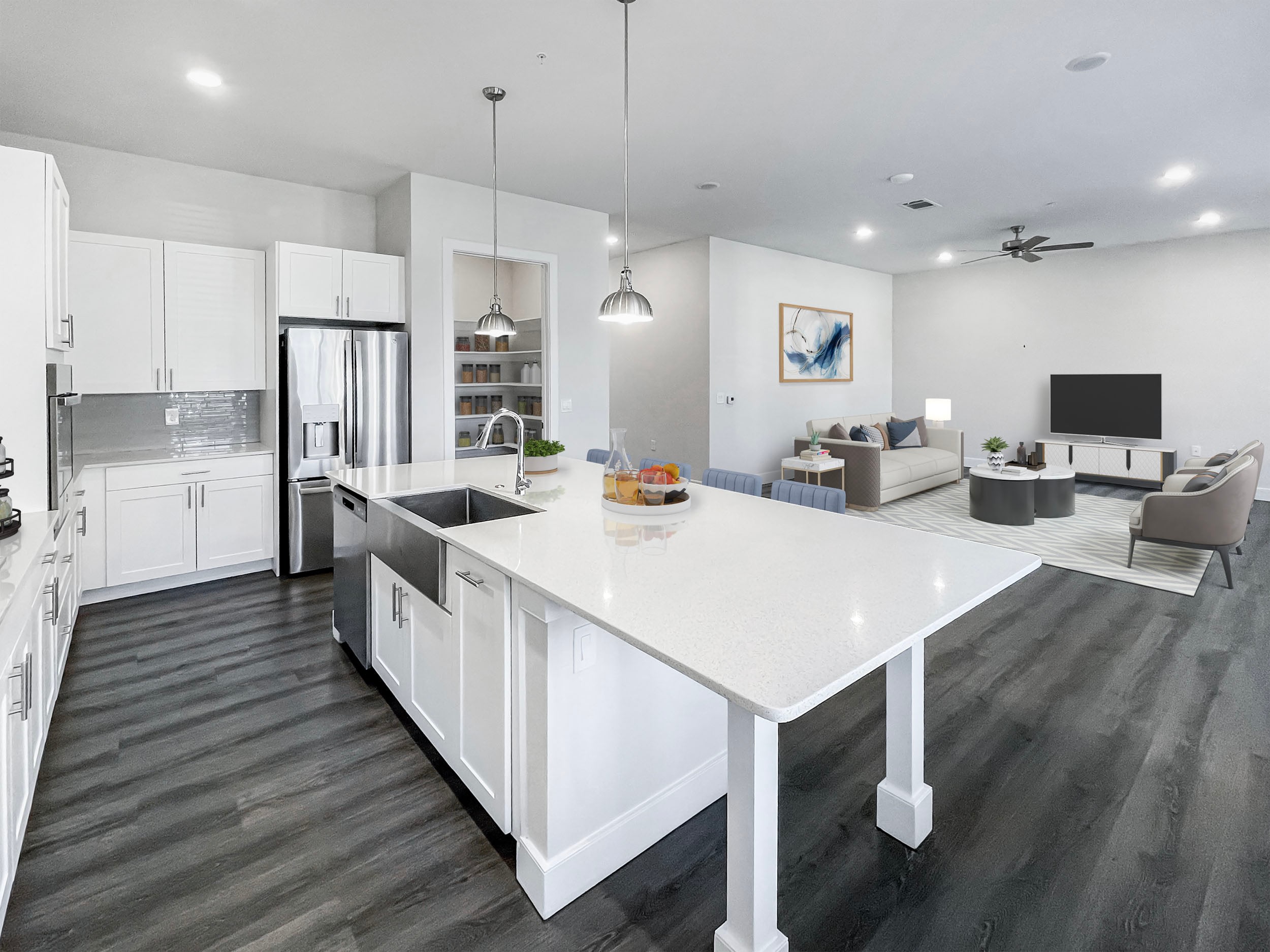 Modern kitchen and living room in an open-concept layout featuring white cabinetry, stainless steel appliances, a large island with a quartz countertop, and stylish pendant lighting, seamlessly connecting to a cozy living area with contemporary furnishings and decor.