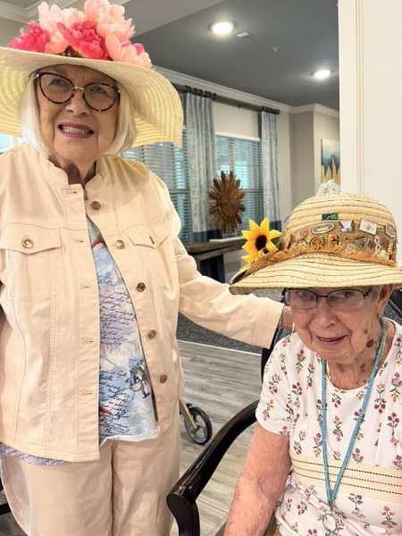 Two smiling elderly women wearing decorated hats indoors