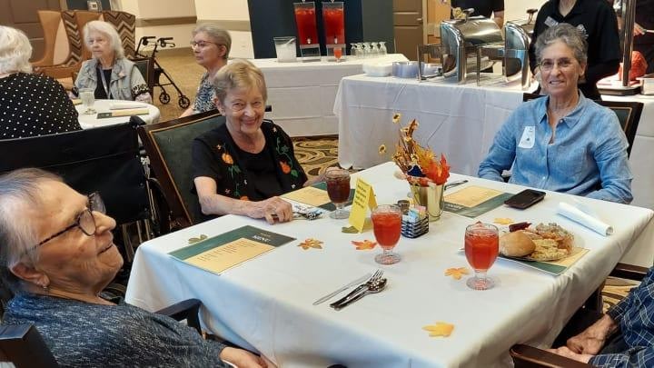 Elderly residents sitting at dining tables with meals and drinks