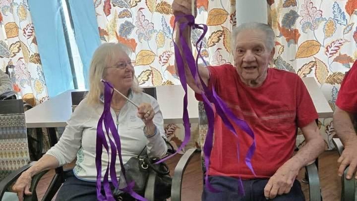 Seniors enjoying a creative activity with purple ribbons in a cheerful community center setting, promoting engagement and social interaction among older adults.