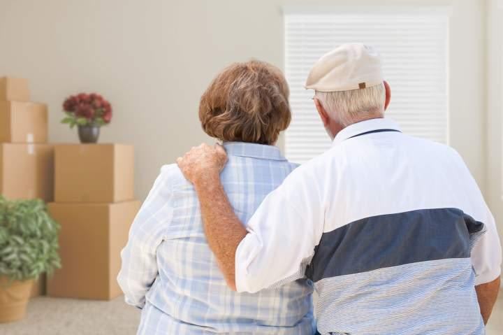 Senior couple from behind looking at their new home with moving boxes nearby
