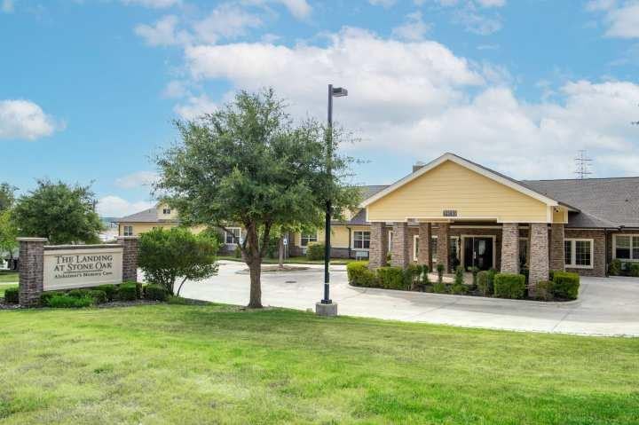 Exterior view of The Landing at Stone Oak facility with yellow and stone facade, landscaping, and signage
