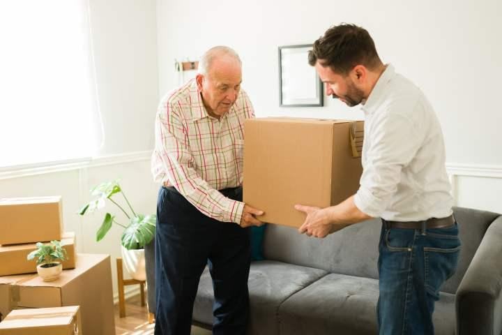 Older man and younger man carrying a box together in a living room