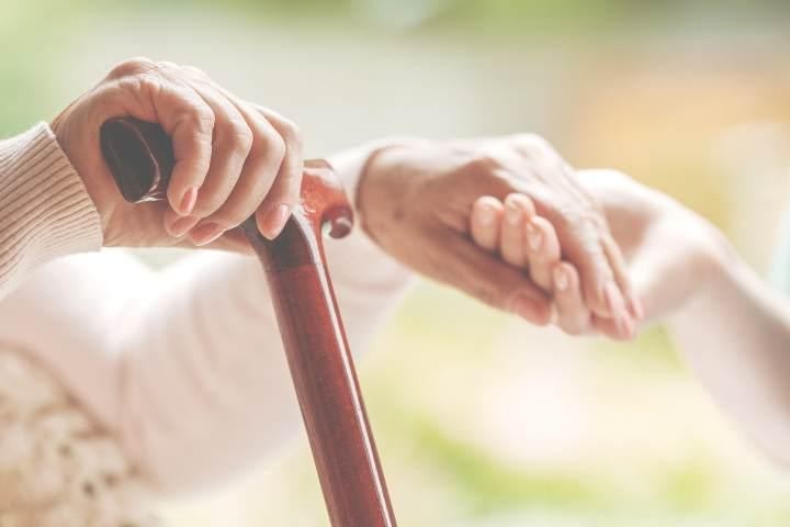 Close-up of elderly hands holding a walking cane with another person's hands offering support