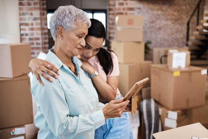 Senior woman with gray hair and younger woman looking at a photo together, surrounded by moving boxes