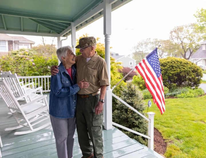 Elderly veteran couple embracing on porch with American flag