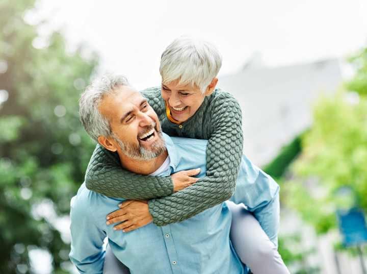 Happy senior couple embracing outdoors, man giving woman a piggyback ride