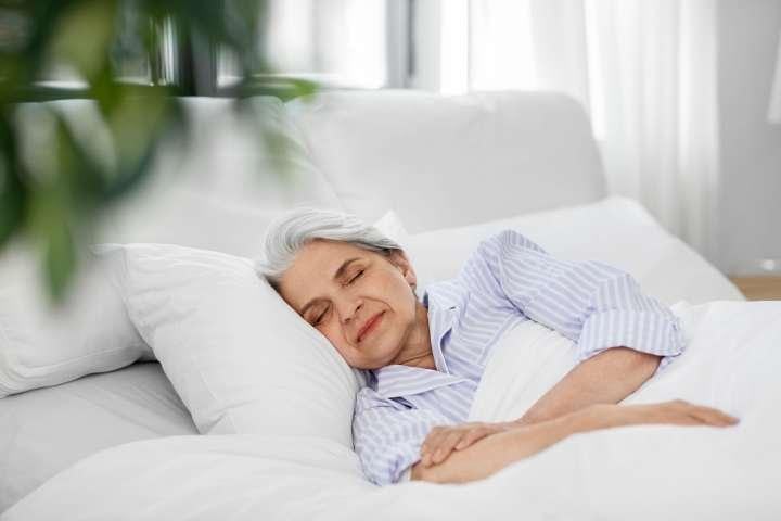 Senior woman sleeping peacefully in white bedding wearing striped pajamas